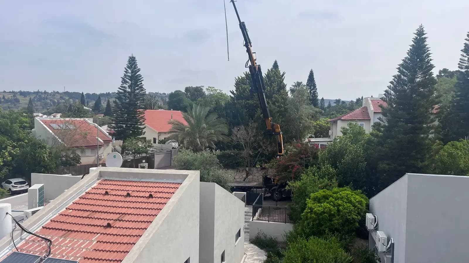 זרוע מנוף מעל גגות בשכונת מגורים בזמן עבודת עצים עירונית